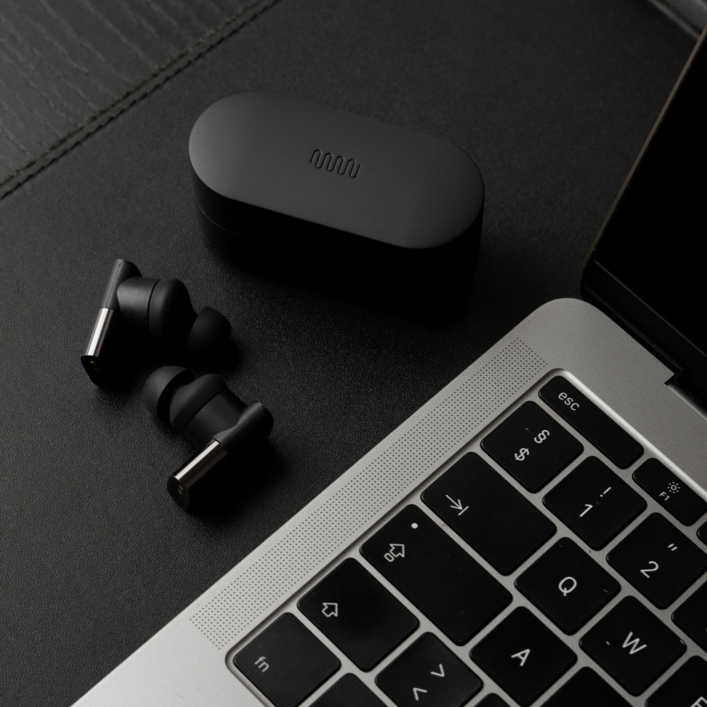 Between 3ANC earbuds on desk next to laptop computer