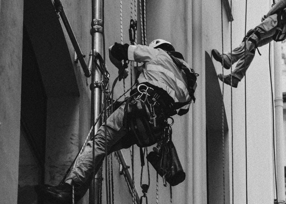 Construction workers suspended from building in black and white